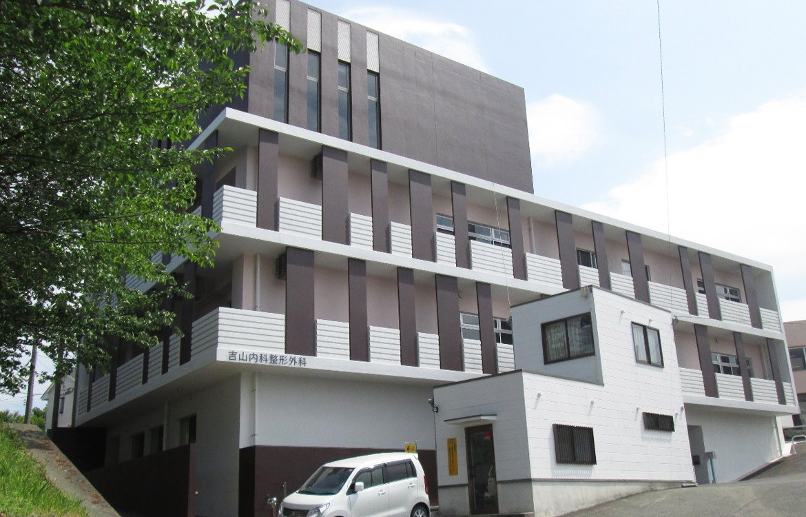 介護施設の建物外観。モダンな3階建て構造で、緑に囲まれた立地。