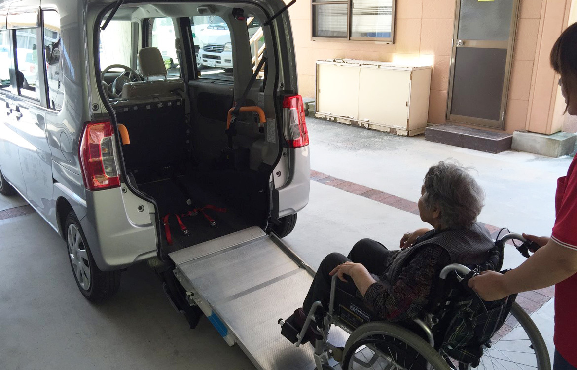 介護施設の玄関で車椅子利用者が福祉車両に乗降している様子